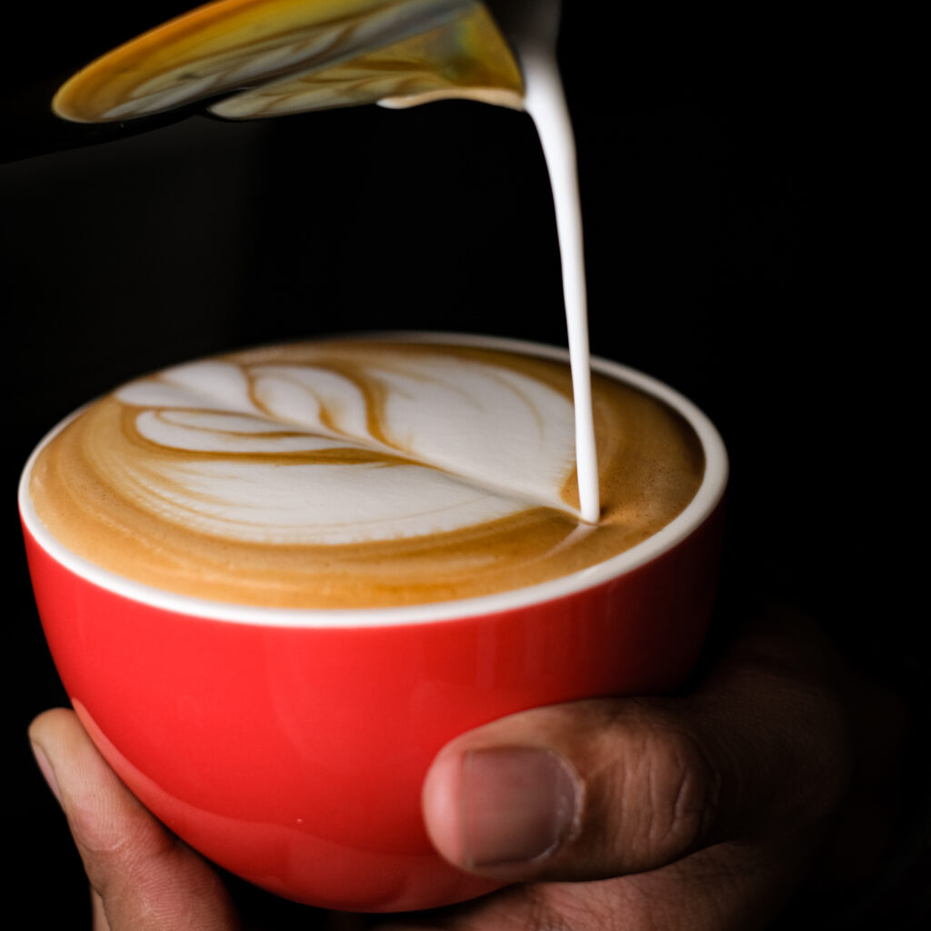 pouring a frothed milk to a cup of cappuccino